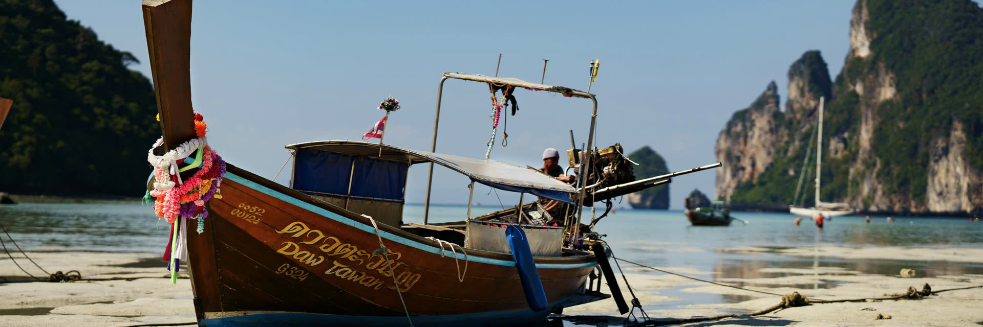 Barca longtail varada en la playa, con los acantilados detrás