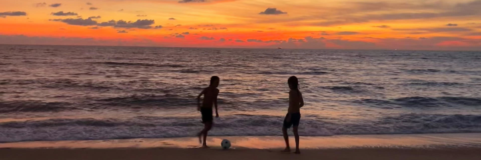 Dos siluetas juegan al fútbol en la orilla al atardecer